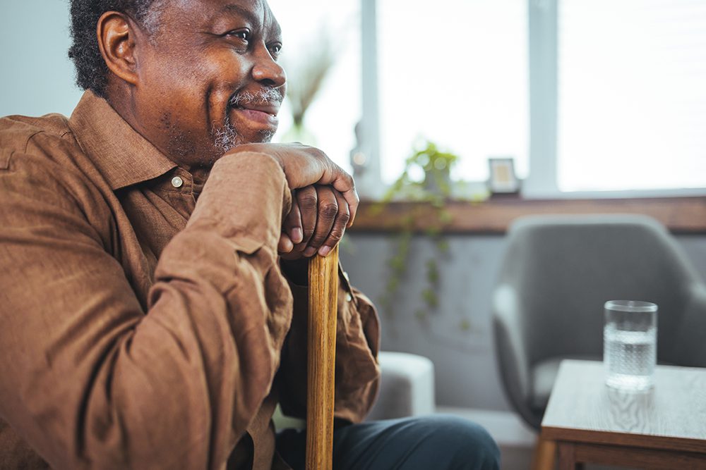 a man staring at something out of frame and smiling while he rests his hands on top of his walking stick